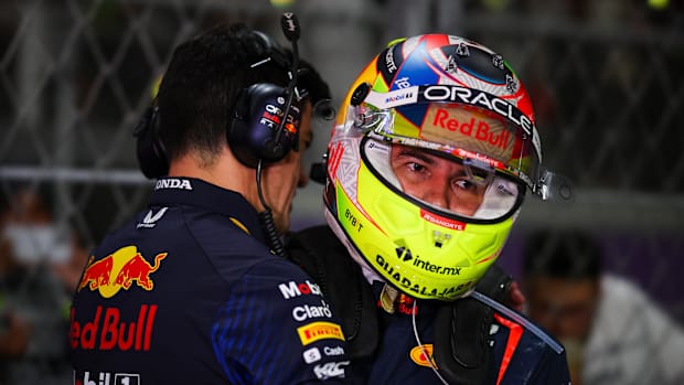 Hombre le dice algo al oído a Checo Pérez mientra trae su casco de piloto.
