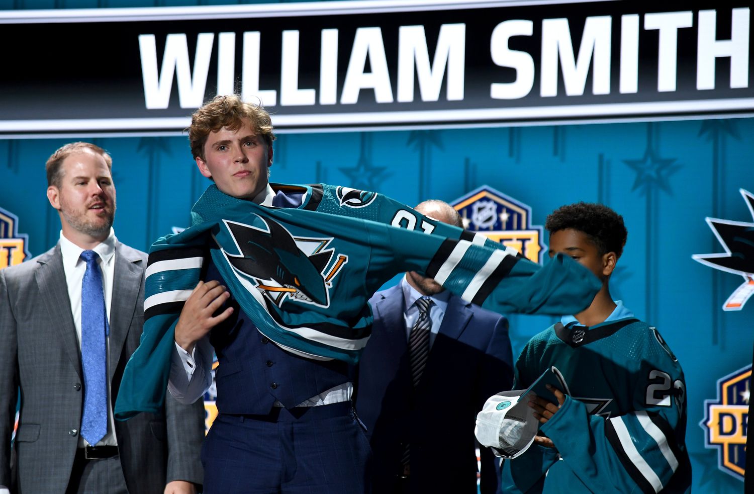 William Smith puts on a San Jose Sharks sweater after being selected with the fourth pick in round one of the 2023 NHL Draft at Bridgestone Arena.