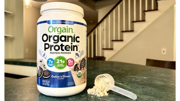 A tub of Orgain organic protein powder in Cookies 'n Cream flavor on a granite countertop