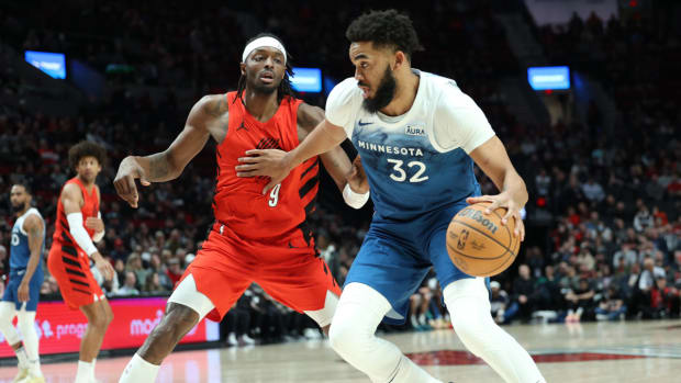 Feb 13, 2024; Portland, Oregon, USA; Minnesota Timberwolves center Karl-Anthony Towns (32) dribbles the ball past Portland Trail Blazers forward Jerami Grant (9) in the first quarter at Moda Center.