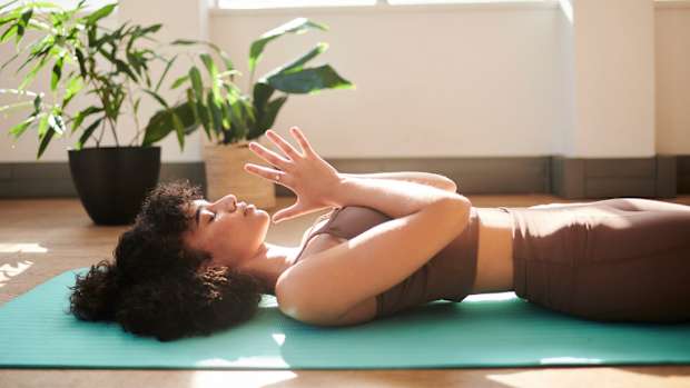 woman in brown workout outfit laying on blue workout grounding mat with hands in prayer