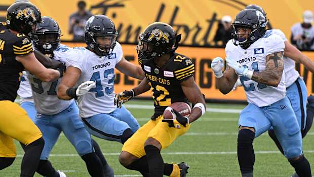 Sep 5, 2022; Hamilton, Ontario, CAN; Hamilton Tiger-Cats slotback Tim White (12) runs with the ball against Toronto Argonauts linebacker Trevor Hoyte (43) and defensive back Daniele Adeboboye (21) in the first half of the annual Labor Day Classic at Tim Hortons Field. Mandatory Credit: Dan Hamilton-USA TODAY Sports