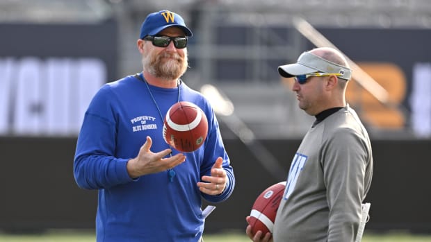 Nov 16, 2023; Hamilton, Ontario, CAN; Winnipeg Blue Bombers head coach Mike O'Shea flips a football as he speaks with special teams co-ordinator Paul Boudreau during practice at Tim Hortons Field. Mandatory Credit: Dan Hamilton-USA TODAY Sports  