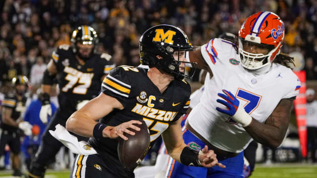 Missouri Tigers quarterback Brady Cook (12) runs the ball as Florida Gators defensive lineman Chris McClellan (7) defends during the first half at Faurot Field at Memorial Stadium.