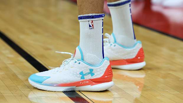 View of white, teal, and orange Under Armour shoes.