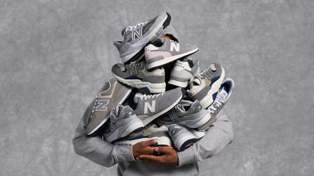 Model holding up several grey New Balance sneakers.
