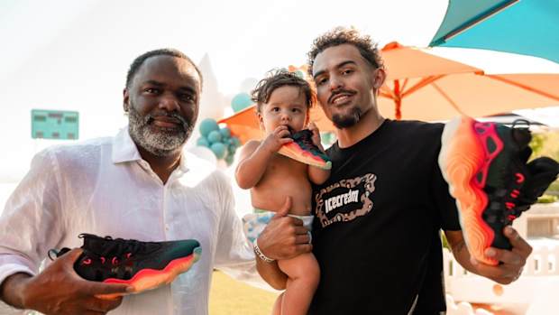 Trae Young alongside his father and son hold black and red adidas shoes.