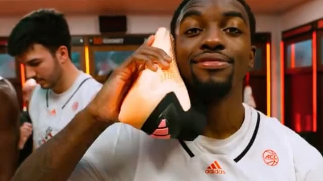 A Miami Hurricanes basketball holds up an orange adidas basketball shoe.