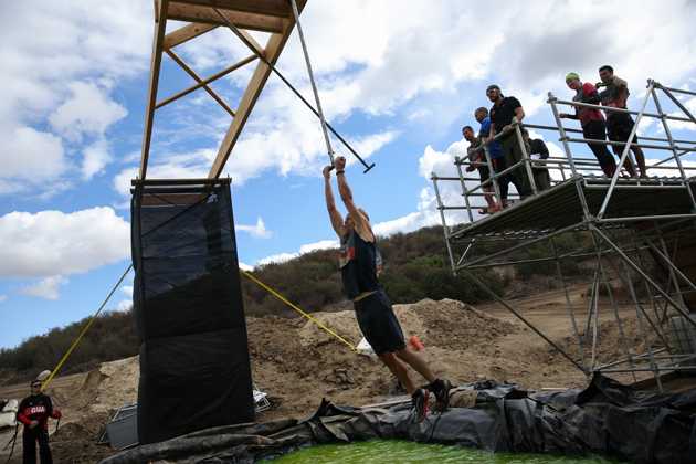 Murphy hangs on during Tough Mudder test obstacle, Swingers.
