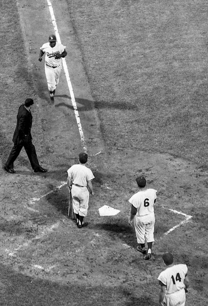 Brooklyn Dodgers second baseman Jackie Robinson (42) approaches his teammates, right fielder Carl Furillo (6) and first baseman Gil Hodges (14), and home plate umpire Bill Engeln while jogging to home plate for an attempt at-bat against the Milwaukee Braves on Thursday, August 2, 1956, in Brooklyn, N.Y. Brooklyn defeated Milwaukee, 3-0.
