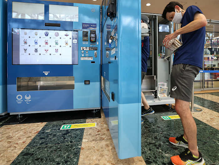 A customer buys an item from a vending machine at the Tokyo Olympics.