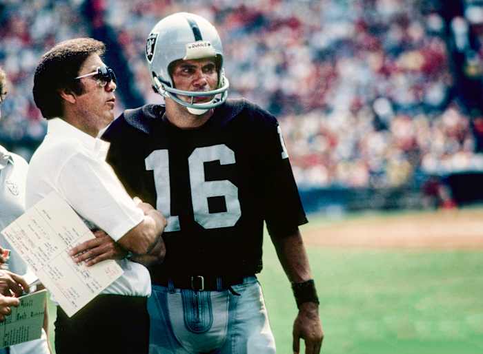 Tom Flores and Jim Plunkett talk on the sideline during a game in 1982