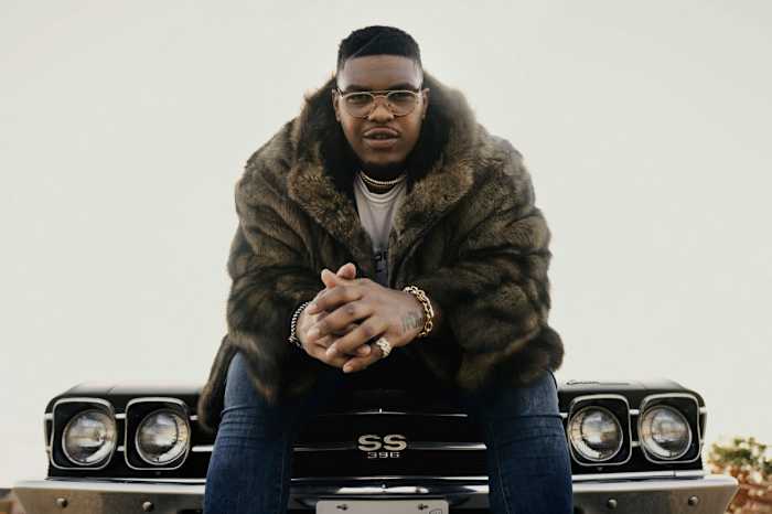 Orlando Brown Jr. poses for a portrait sitting and leaning forward on the hood of a car