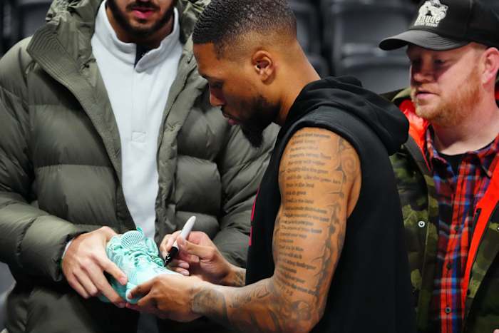 Damian Lillard signs a fan's shoe before a game.