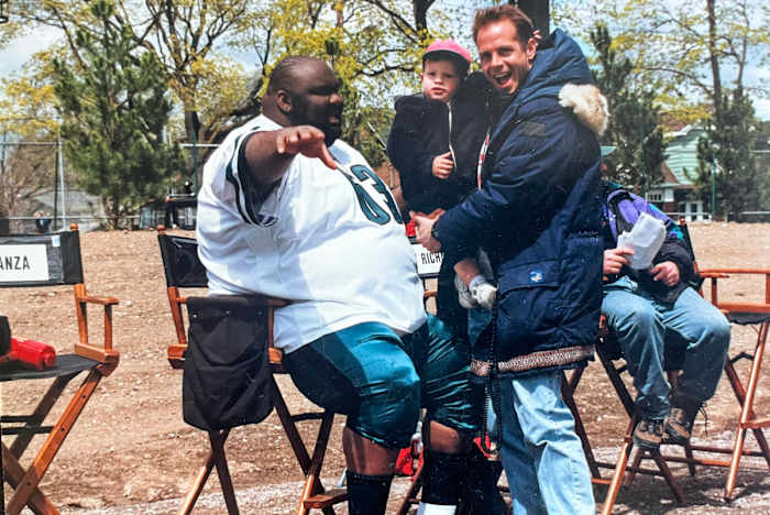 Actor Jaime Cardriche and screenwriter Tim Kelleher, holding his son, talk on set of “The Garbage Picking Field Goal Kicking Philadelphia Phenomenon”