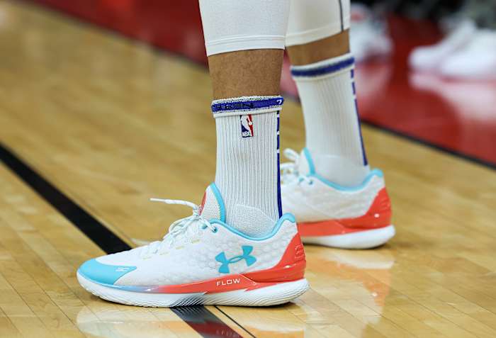 View of white, teal, and orange Under Armour shoes.