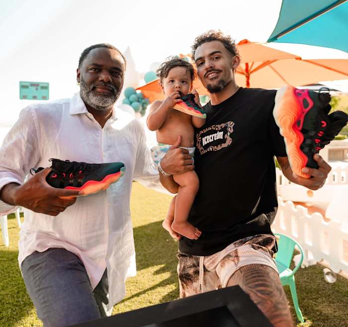 Trae Young alongside his father and son hold black and red adidas shoes.