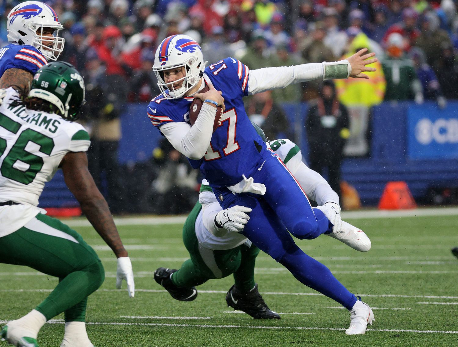 Josh Allen runs with the ball in one hand while a Jets player reaches for his legs to tackle him