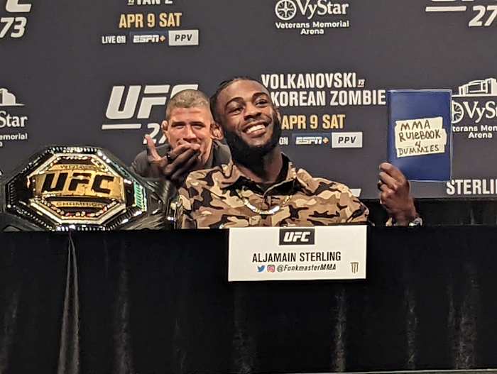Bantamweight champion Aljamain Sterling holds an "MMA Rulebook 4 Dummies" to taunt interim champion Petr Yan (not pictured) during a press conference at UFC 273.