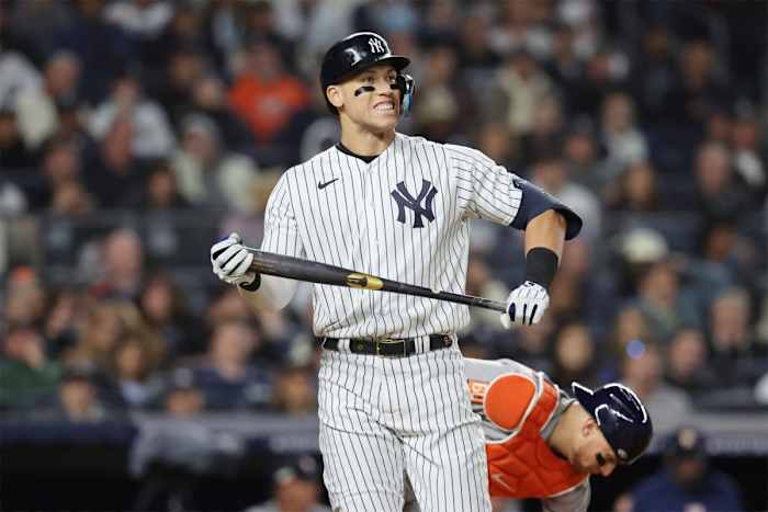 Yankees star slugger Aaron Judge stands on the field holding a bat and smiling
