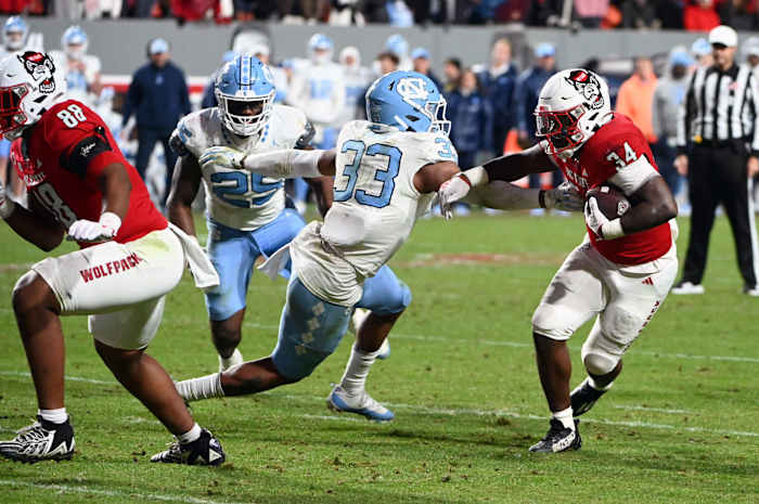 Nov 25, 2023; Raleigh, North Carolina, USA; North Carolina State Wolfpack running back Delbert Mimms III (34) runs against North Carolina Tar Heels linebacker Cedric Gray (33) during the second half at Carter-Finley Stadium. Mandatory Credit: Rob Kinnan-USA TODAY Sports