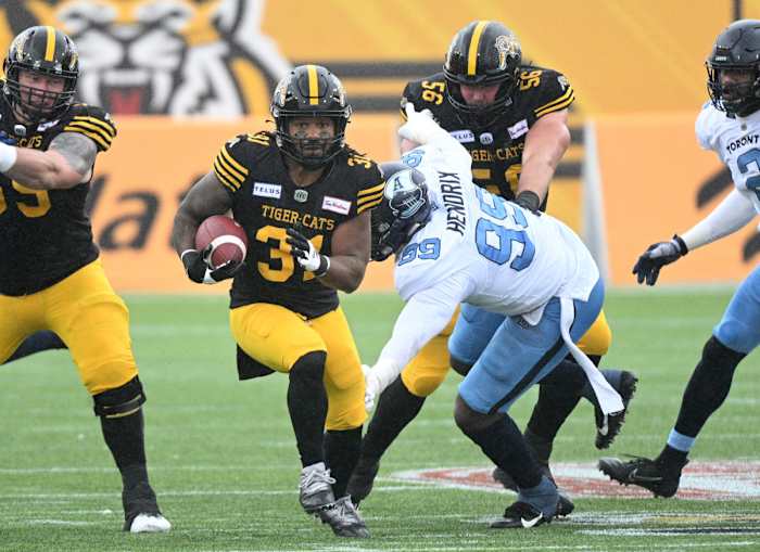 Sep 5, 2022; Hamilton, Ontario, CAN; Hamilton Tiger-Cats running back Sean Thomas Erlington (31) carries the ball past Toronto Argonauts lineman Dewayne Hendrix (99) in the first half of the annual Labor Day Classic at Tim Hortons Field. Mandatory Credit: Dan Hamilton-USA TODAY Sports