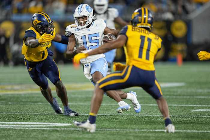 Dec 27, 2023; Charlotte, NC, USA; North Carolina Tar Heels quarterback Conner Harrell (15) runs for yards tackled by West Virginia Mountaineers cornerback Beanie Bishop Jr. (11) and linebacker Lee Kpogba (1) during the first half at Bank of America Stadium. Mandatory Credit: Jim Dedmon-USA TODAY Sports
