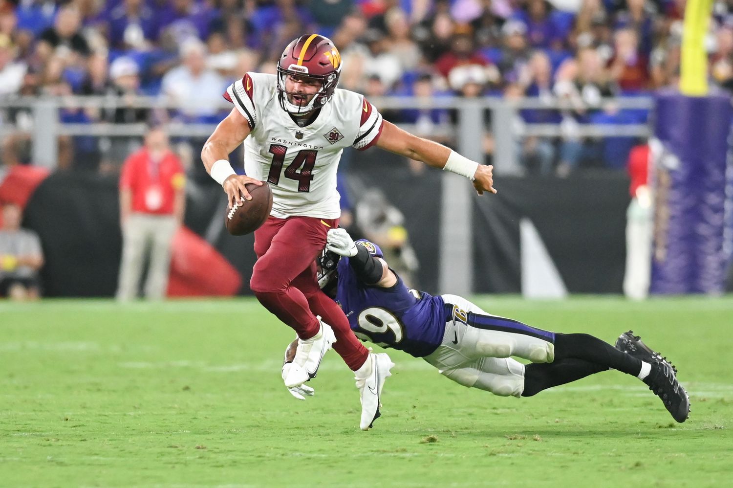 Washington Commanders quarterback Sam Howell (14) scrambles away from a diving Baltimore Ravens safety Ar'Darius Washington (29) during the second half at M&T Bank Stadium.