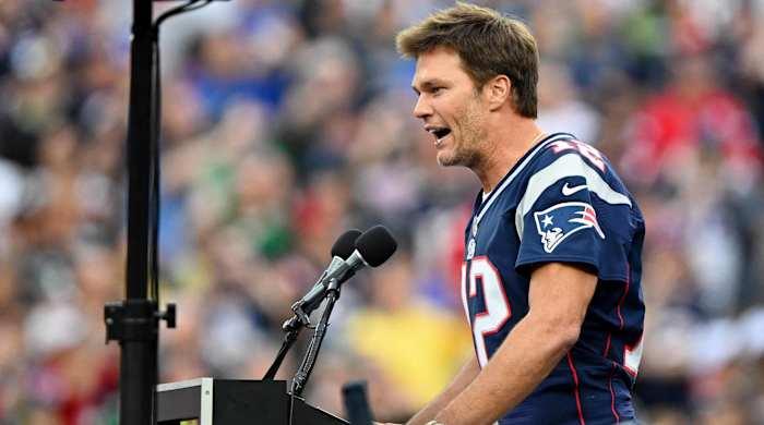 Former Patriots quarterback Tom Brady speaks to the New England crowd at a podium while being honored at halftime of a game.