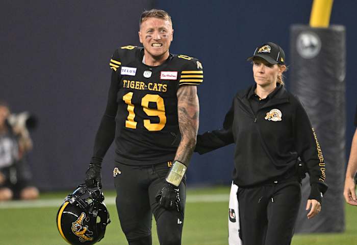 Jun 18, 2023; Toronto, Ontario, CAN; Hamilton Tiger-Cats quarterback Bo Levi Mitchell (19) is escorted off the field by team head therapist Claire Tofflemire after suffering an injury against the Toronto Argonauts in the fourth quarter at BMO Field. Mandatory Credit: Dan Hamilton-USA TODAY Sports