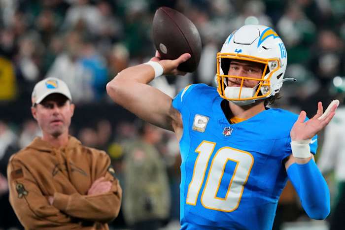 Justin herbert throws while Brandon Staley watches from behind him