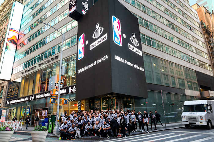 Foot Locker employees pose for a picture beside an NBA billboard.