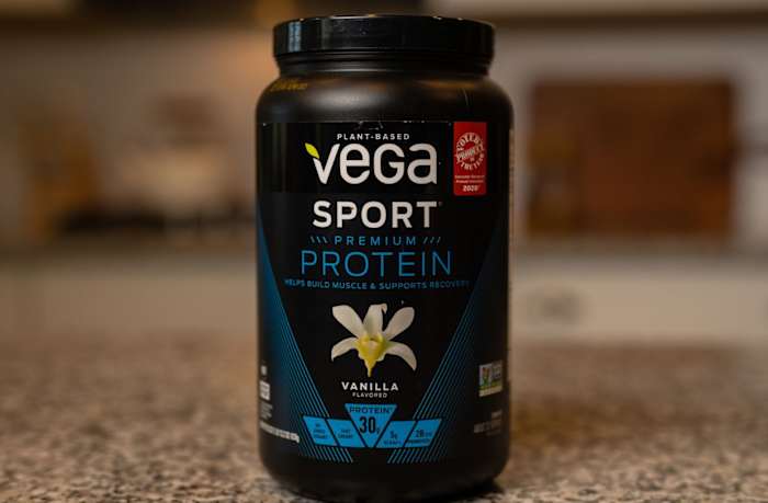 Black tub with blue and white writing that says "Vega Sport Premium Protein" on a counter
