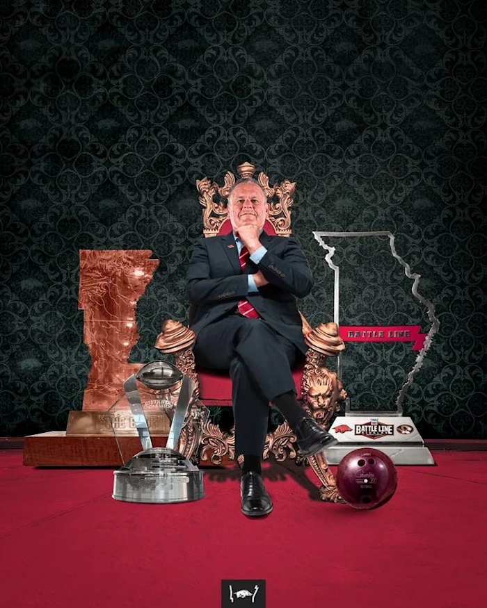 Sam Pittman sits on a throne surrounded by all the trophies his Razorbacks won in 2021, along with Larry the Bowling Ball.