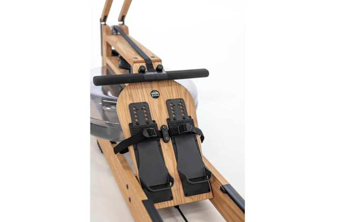 A close up image of the WaterRower machine in a light wood stain and black foot straps
