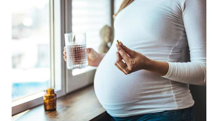 Pregnant woman holding a prenatal vitamin and glass of water
