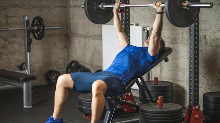 Man bench pressing barbell with weight plates on an inclined weight bench
