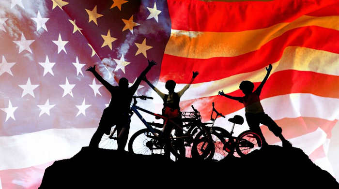 Silhouette of a family next to bicycles in front of a large American flag
