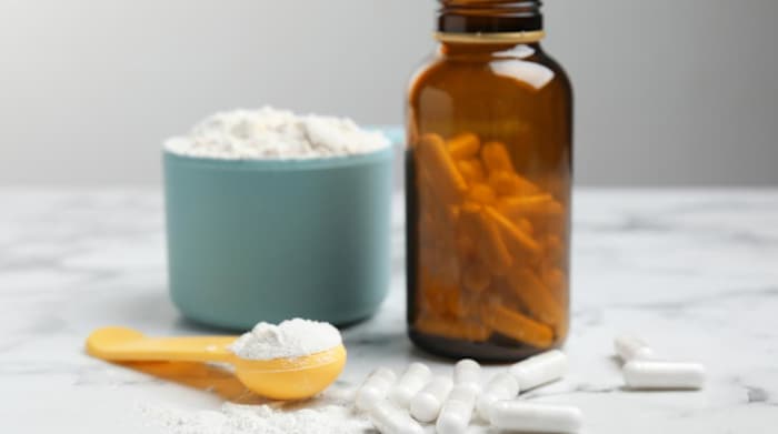 A bottle of white capsules and a teaspoon of white powder