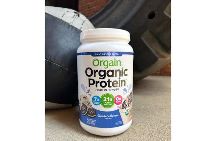 A tub of Orgain organic protein powder in Cookies 'n Cream flavor on the floor of a Crossfit gym
