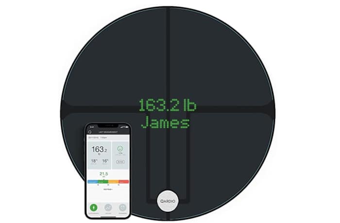 The circular Qardio Base 2 bathroom scale next to a smartphone opened to the Qardio app
