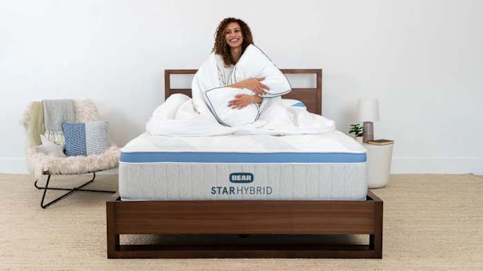 A woman lies on top of a Bear Star Hybrid Mattress hugging a pillow.
