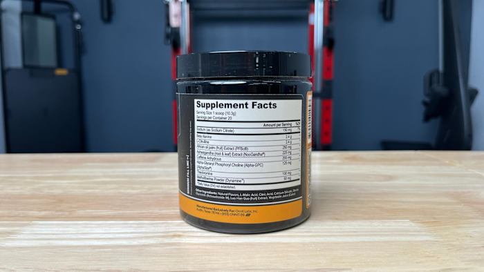 The Supplements Facts label of a tub of Onnit Alpha Brain Pre-Workout powder on a wooden table in a gym
