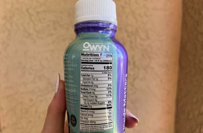 A person holding a bottle of OWYN Plant-Based Protein Shakes and showing the Nutrition Facts label