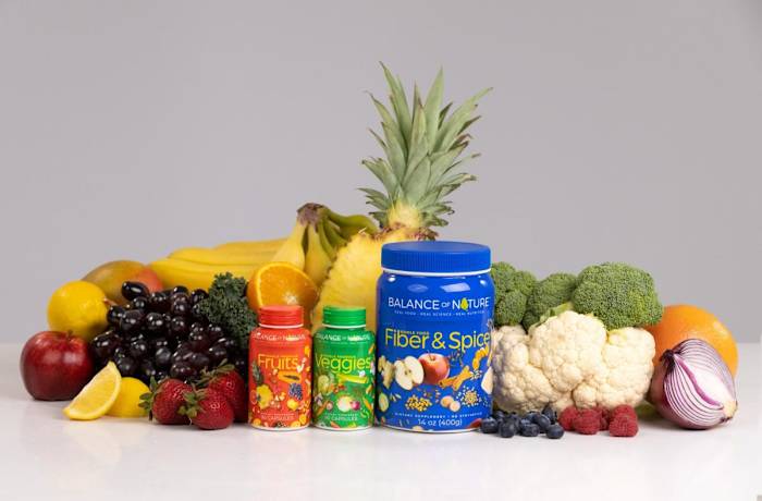 Brightly colored Balance of Nature Fruits, Veggies, and Fiber and Spice supplement containers surrounding by fresh fruit and vegetables