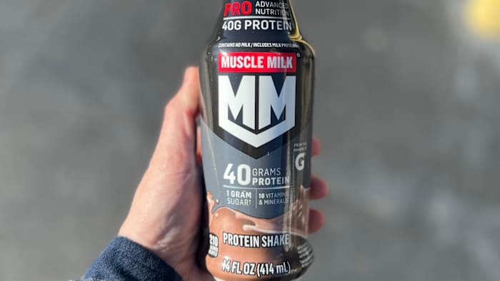 A hand holding a Muscle Milk Pro Advanced Nutrition protein shake bottle