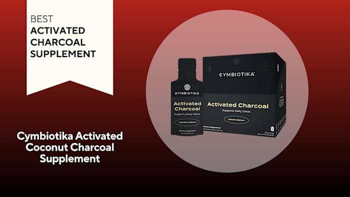 A black and gold box and packet of Cymbiotika Activated Coconut Charcoal Supplement against a red background