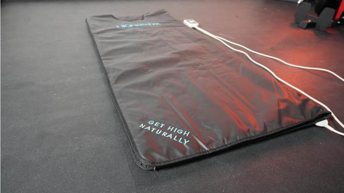 Image of black Higherdose Infrared Sauna Blanket laid out on a black floor with blue text  that reads "get high naturally"