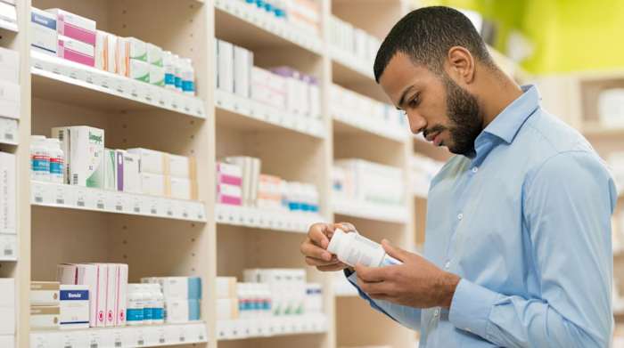 A man in a blue shirt holding a bottle of probiotic supplements as he stands in front of a shelf full of similar products