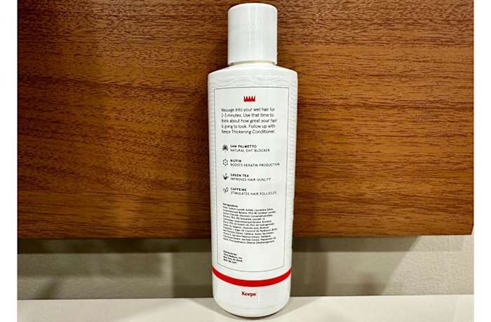 The back side of Keeps Thickening Shampoo bottle against a wood backdrop.